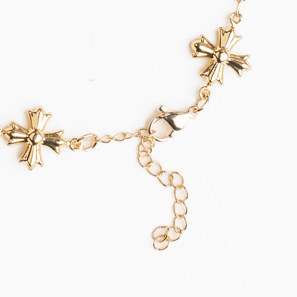 
                  
                    Gold bracelet with cross shaped charms on a white background
                  
                