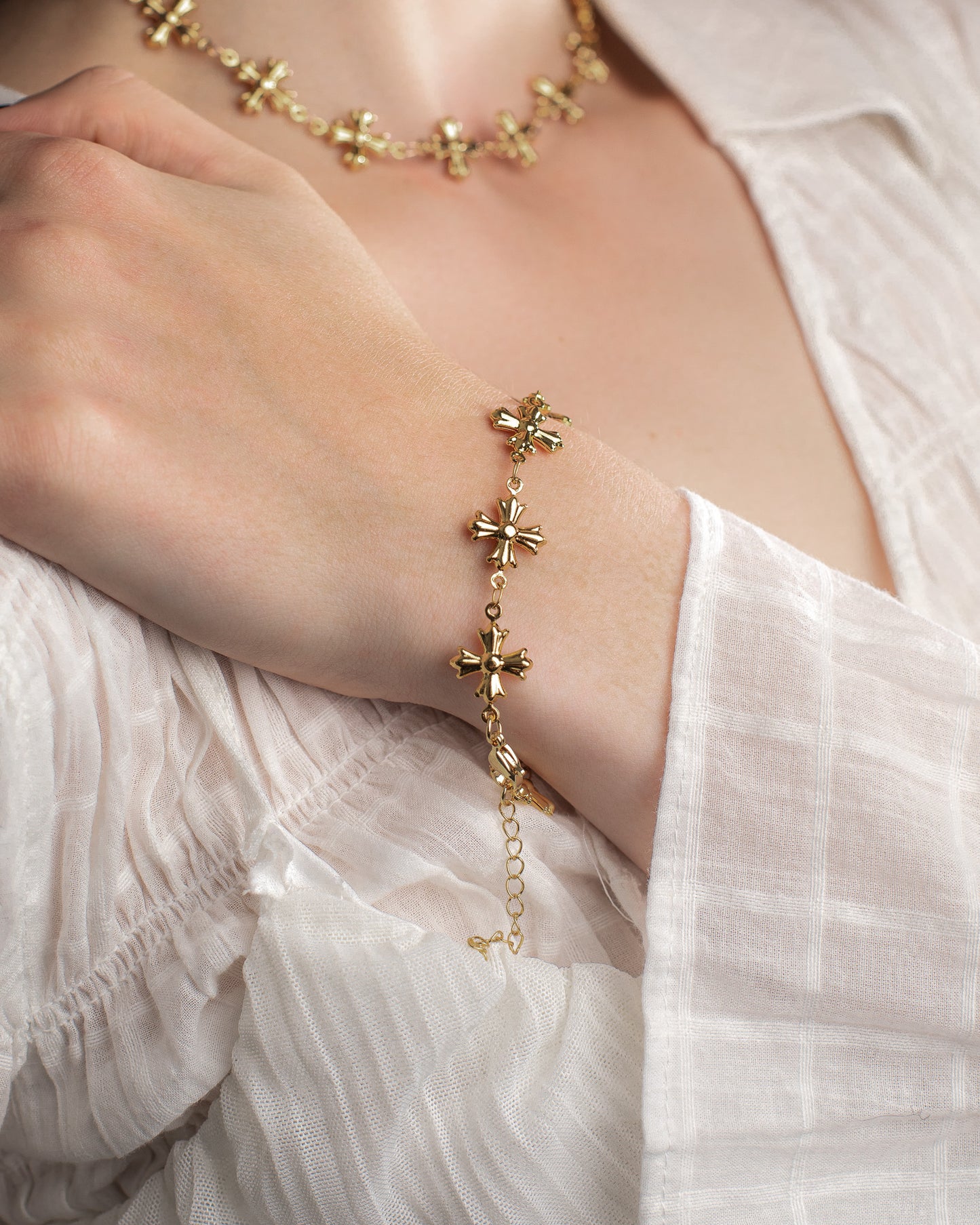 Gold dainty bracelet with cross designs on a person wearing a white blouse.