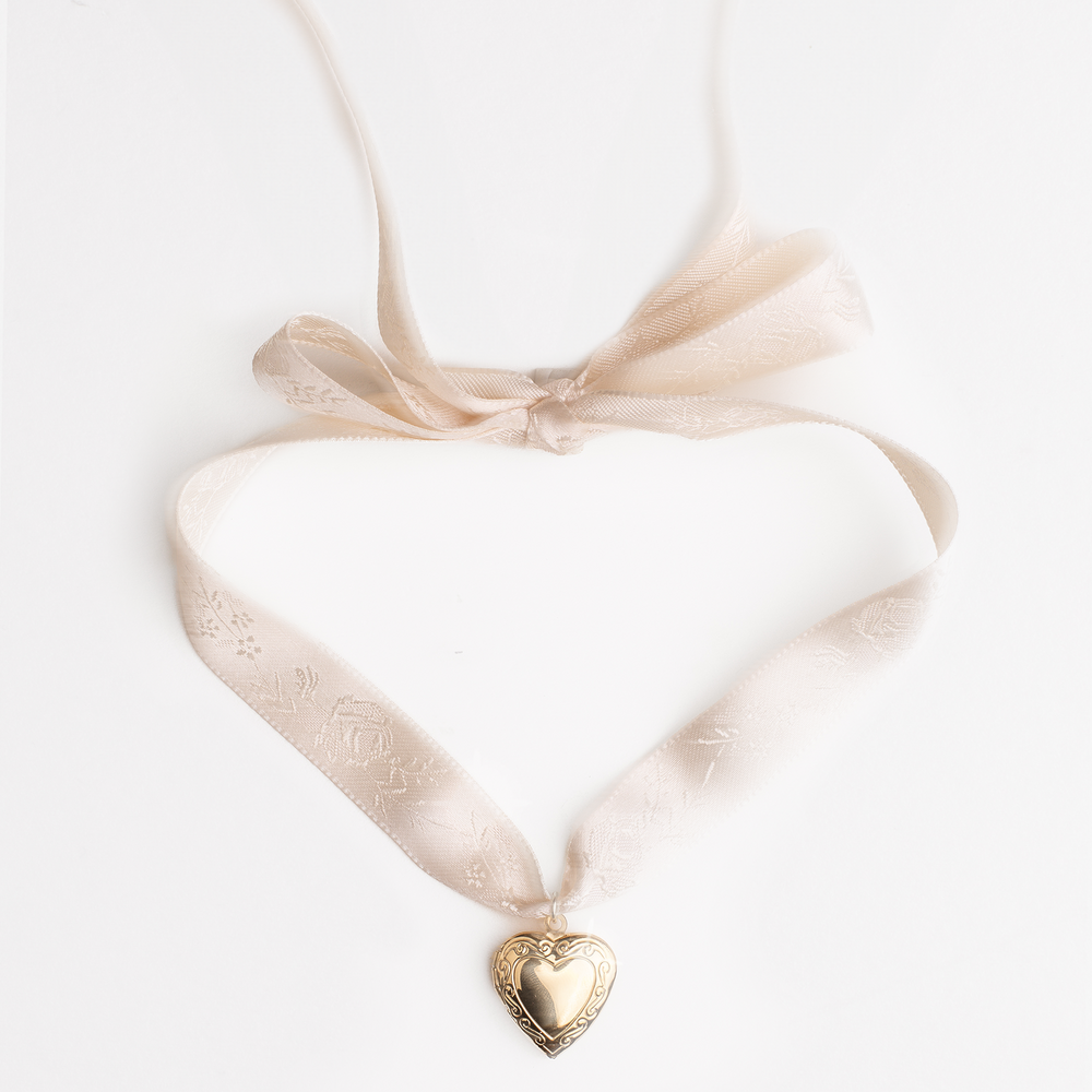 Vintage heart locket gold pendant on a cream satin ribbon against a white background