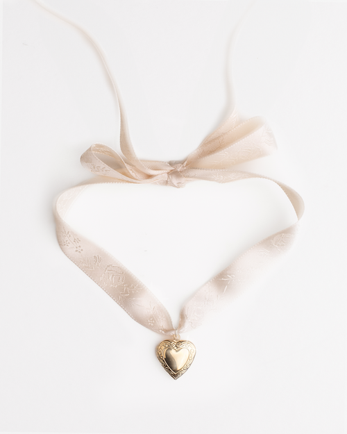 Vintage heart locket gold pendant on a cream satin ribbon against a white background