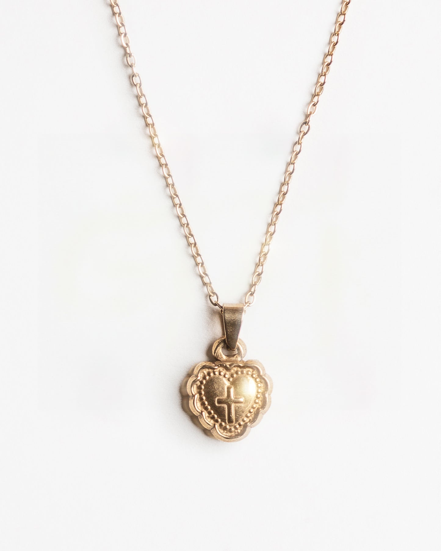 Gold heart shaped pendant necklace with a cross design on a white background